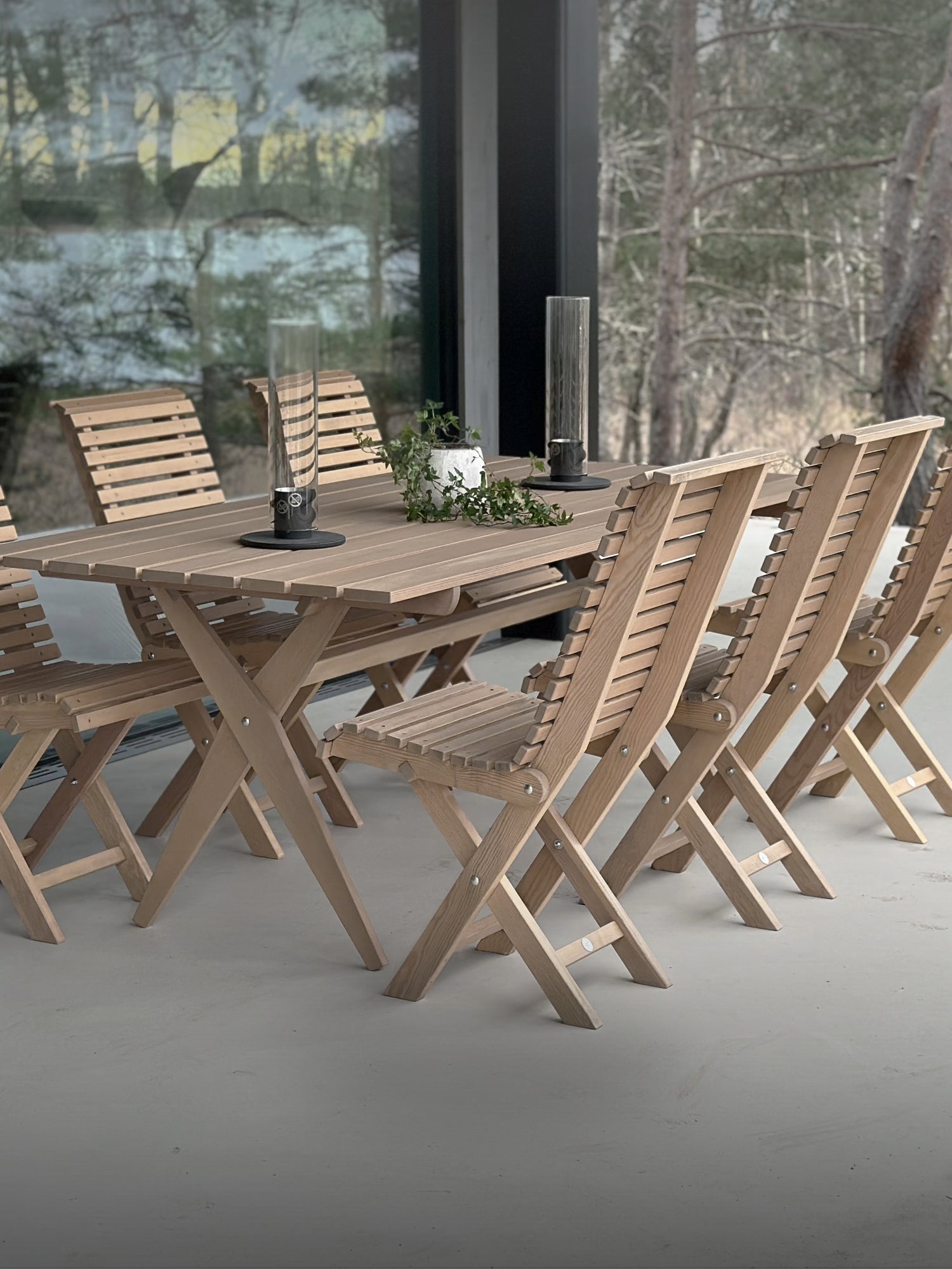 Naturfärgade hopfällbara trädgårdsmöbler – stilrent matbord med stolar, placerat på en modern uteplats med panoramafönster och skandinavisk design