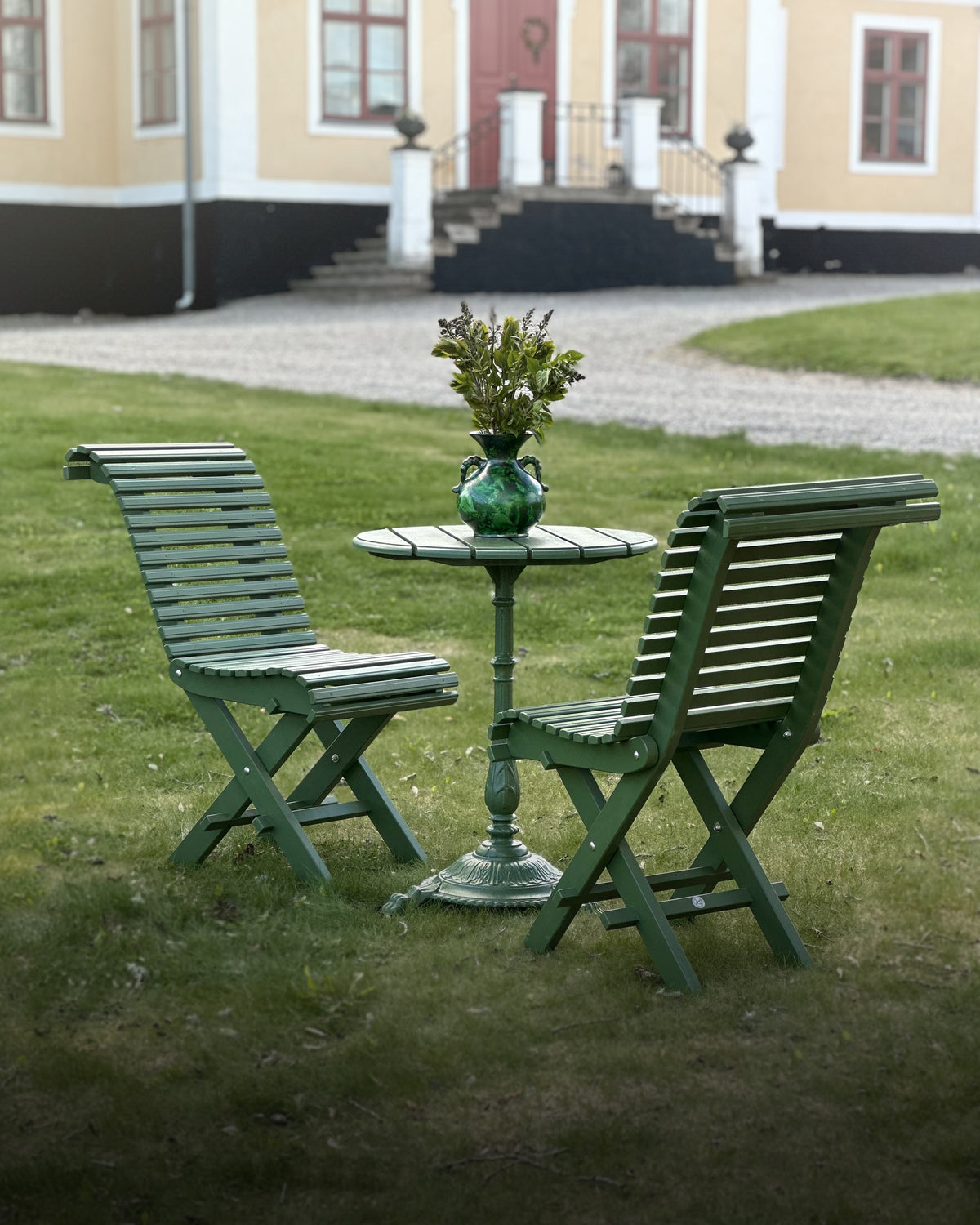 Cafebord med två gröna stolar på Långbro Gård, trädgårdsmöbler för uteservering.